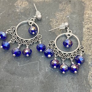 May include: Silver dangle earrings with a circular design and blue iridescent glass beads.