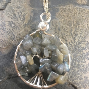 Op de afbeelding: Een zilveren draadgewikkelde levensboom hanger met een zilveren ketting. De boom is versierd met iriserende labradorite stenen.