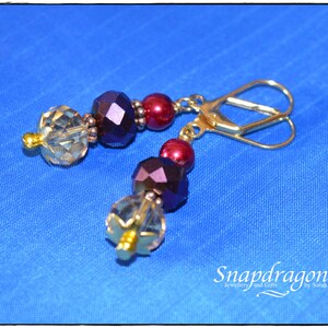 May include: Gold earrings with burgundy and clear faceted glass beads. The earrings have a hook closure.
