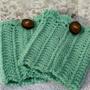 May include: Three crocheted leg warmers in a light green color with brown wooden buttons.