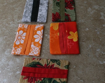 May include: Five fabric tissue holders with different floral patterns. The holders are made of cotton fabric and have a rectangular shape. The patterns include black and white flowers, green leaves with red flowers, orange and yellow flowers, and a red and orange floral pattern.
