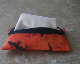 May include: A tissue box cover with a black trim and an orange and brown fabric with a black silhouette of a creature on it.