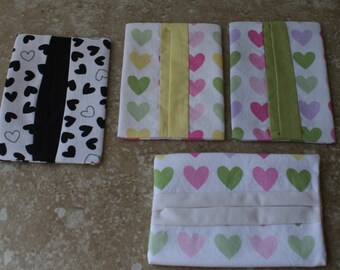 May include: Four tissue box covers with different heart patterns. The covers are made of fabric and have a white background with pink, green, and yellow hearts. One cover has a black and white heart pattern.