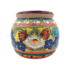 May include: A round ceramic pot with a tan base, featuring hand-painted orange and black butterflies, white daisies, and blue flowers. The design includes horizontal bands of red, green, and yellow, with a dark red rim and white scrollwork.