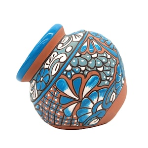May include: A hand-painted ceramic pot with a brown base and a blue rim. The pot is decorated with blue, white, and teal floral patterns. The design includes stylized flowers and geometric shapes.