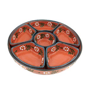 May include: A terracotta-colored serving dish set with a central bowl and six surrounding compartments. Each section is decorated with white floral patterns and green leaves, outlined with a dark blue trim. The set is designed for serving appetizers or snacks.