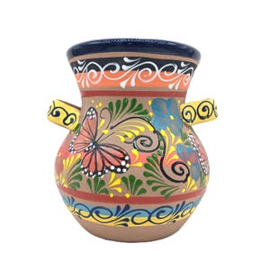 May include: A hand-painted ceramic vase with a wide mouth and two small handles. The vase features a brown base with colorful butterfly and floral designs in red, yellow, blue, and green. The rim is dark blue with orange and white accents.