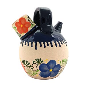 May include: A blue and white ceramic pitcher with a floral design. The pitcher has a small spout and a handle. The floral design features red, blue, green, and yellow flowers.