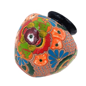 May include: A hand-painted ceramic vase with a black rim and a colorful floral design. The vase features a vibrant mix of orange, green, red, and blue flowers, with intricate details and patterns. The background is white.