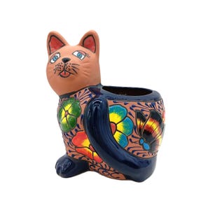 May include: A ceramic cat-shaped planter with a brown body and a dark blue tail. The planter is decorated with colorful floral patterns in yellow, red, green, and blue. The cat has blue eyes and a smiling expression.