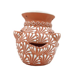 May include: Terracotta-colored ceramic pot with white floral patterns. The pot has a wide base, a narrower neck, and a white rim. The design includes cut-out openings and is suitable for home decor.