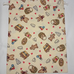 May include: A drawstring bag made of cream-colored fabric with a gingerbread man, heart, basket, and cookie cutter pattern.