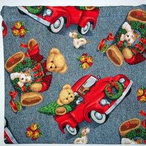 May include: A red truck with a wreath on the front, teddy bears with wreaths around their necks, and jingle bells on a blue denim background.