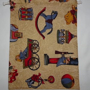 May include: A beige drawstring bag with a whimsical toy theme. The bag features a variety of toys including a rocking horse, a toy soldier, a toy drum, a toy wagon, a carousel, and a teddy bear. The bag is perfect for storing small items or gifts.
