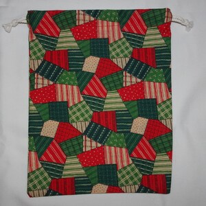 May include: A drawstring bag with a patchwork design in red, green, and beige. The fabric features geometric shapes with various patterns, including stripes, dots, and plaid. The bag has a white drawstring closure.