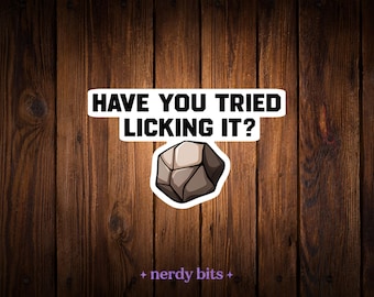May include: A die-cut sticker featuring a cartoon illustration of a gray, multi-faceted rock positioned below the bold, black, sans-serif text that reads, HAVE YOU TRIED LICKING IT? The sticker has a white border and is centered on the image.