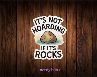 May include: A sticker featuring a brown rock illustration centered on a light blue watercolor splash. The text reads IT'S NOT HOARDING IF IT'S ROCKS in bold black capital letters. The sticker has a white border and a matte finish.