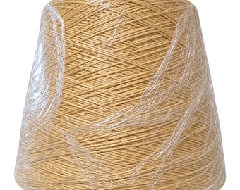 May include: A large, conical spool of light tan yarn wrapped in clear, crinkled plastic film. The yarn is wound tightly in a consistent diagonal pattern around the central core, creating a smooth, uniform texture across the entire surface.