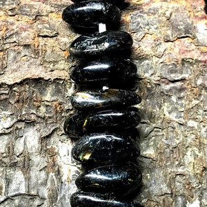 May include: A strand of black gemstone beads with gold flecks. The beads are oval shaped and strung on a white cord.