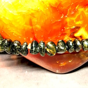 May include: A black gemstone bracelet with smooth, rounded beads. The bracelet is resting on a heart-shaped piece of carnelian.