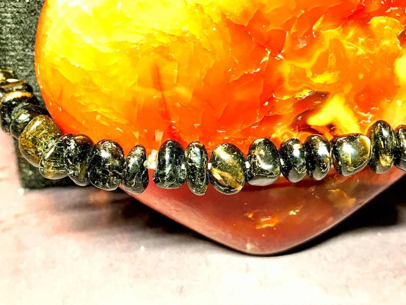 May include: A black gemstone bracelet with smooth, rounded beads. The bracelet is resting on a heart-shaped piece of carnelian.