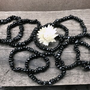 May include: A set of black gemstone bracelets made with small, irregular shaped beads. The bracelets are arranged in a loose pile on a wooden surface.