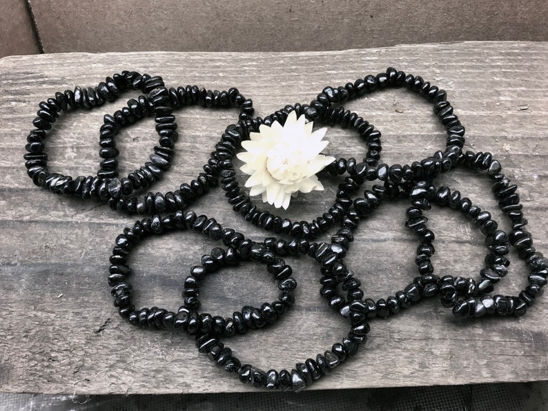 May include: A set of black gemstone bracelets made with small, irregular shaped beads. The bracelets are arranged in a loose pile on a wooden surface.