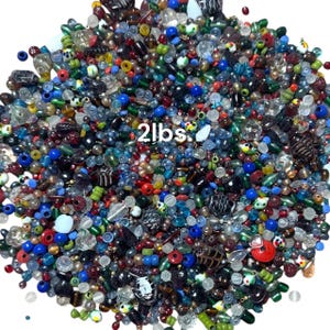 May include: A large pile of colorful beads in various shapes and sizes. The beads are a mix of colors including red, blue, green, and clear. The text "2lbs." is visible in white. These beads are ideal for jewelry making and crafts.