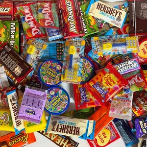 May include: A large assortment of various candy and chocolate products including Hershey's bars, Hot Tamales, Pez dispensers, Dum Dums, Chupa Chups, Sweet Shop tins, and Peeps. The collection features a variety of colorful branded packaging.