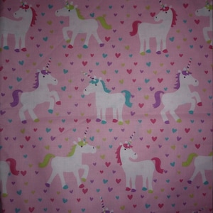 May include: Pink fabric with a repeating pattern of white unicorns with colorful manes and tails. The background is covered in small pink, purple, and blue hearts.