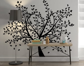 May include: Black silhouette of a tree with leaves on a white wall. A black lamp with a white shade is on the left side of the image. A wooden table with a black metal frame is in front of the tree. There are books and a decorative object on the table.