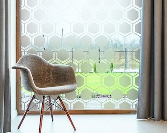 May include: A brown fabric chair with wooden legs sits in front of a window with a honeycomb pattern frosted glass. The window is framed in wood and has gray curtains on either side.