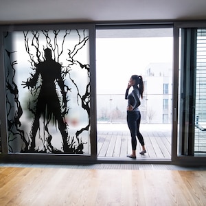 May include: A woman stands on a balcony looking out at a city view. A large, dark silhouette of a creature is visible on the frosted glass door behind her.