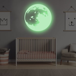 May include: A green glow-in-the-dark moon wall decal, perfect for a nursery or child's room. The decal is shaped like a full moon with a detailed surface texture.
