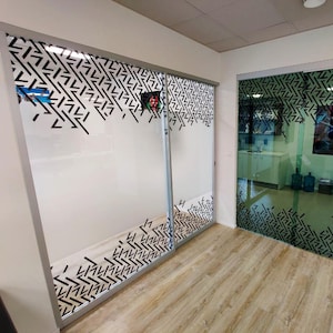 Könnte beinhalten: Zwei Glastüren mit einem schwarz-weißen geometrischen Muster. Die Türen sind mattiert und haben einen Schiebemechanismus. Die Türen befinden sich in einem Büro mit einem Holzboden.