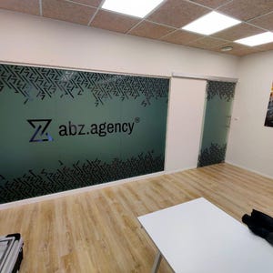 Puede incluir: Un espacio de oficina moderno con una pared de vidrio esmerilado que presenta un patr&oacute;n geom&eacute;trico en blanco y negro y el logotipo "abz.agency".