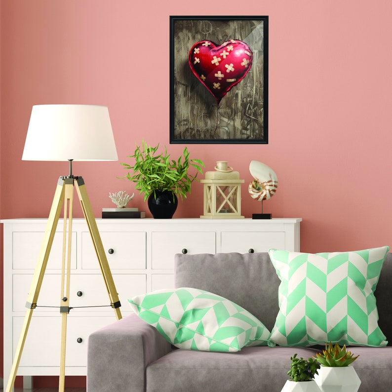 May include: A framed print of a red heart-shaped balloon with white bandages on it, hanging from a string against a textured background.