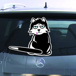 May include: A black and white cartoon husky dog sticker with a pink tongue sticking out. The dog is sitting on its hind legs with its tail sticking out behind it. The sticker is on the back window of a car.