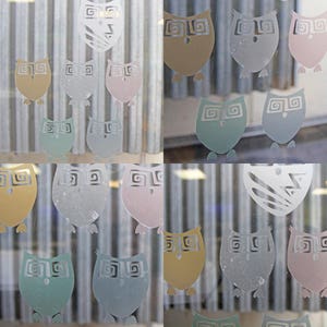 Puede incluir: Una colecci&oacute;n de calcoman&iacute;as con forma de b&uacute;ho en varios colores, incluyendo azul claro, verde claro, rosa claro y beige, se muestran en una superficie de vidrio. Los b&uacute;hos tienen un dise&ntilde;o estilizado con patrones en espiral.