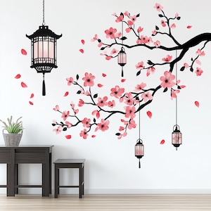 May include: A wall decal featuring a black silhouette of a cherry blossom branch with pink flowers and hanging lanterns. The decal is on a white wall with two dark brown tables in the foreground.