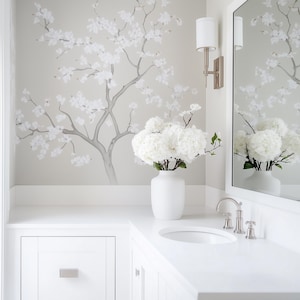 May include: A white bathroom vanity with a white porcelain sink and chrome faucet. A white vase with white flowers sits on the counter. The wall behind the vanity features a gray wallpaper with a white floral design.