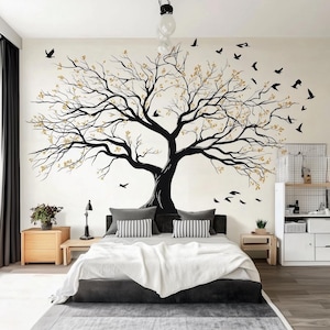 May include: A bedroom featuring a black tree wall decal with gold detailing and flying birds. The bed has grey pillows and a white blanket. Wooden bedside tables and a grey rug complete the room's decor.