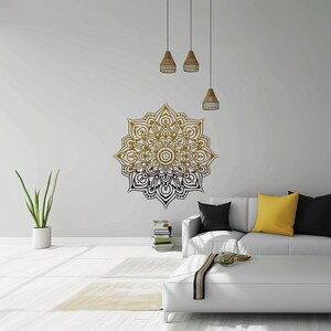 May include: A gold and black mandala wall decal with intricate details, displayed on a white wall in a living room setting with a white couch and a coffee table.