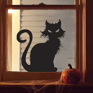 Könnte beinhalten: Eine schwarze Katzensilhouette mit leuchtenden Augen in einem Fenster, die eine gruselige Halloween-Dekoration darstellt. Ein kleiner orangefarbener Kürbis sitzt auf der Fensterbank, verziert mit Spinnweben.