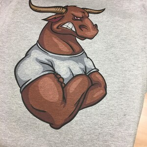 May include: A gray t-shirt with a brown cartoon bull with a white undershirt. The bull has a serious expression and is flexing its muscles.
