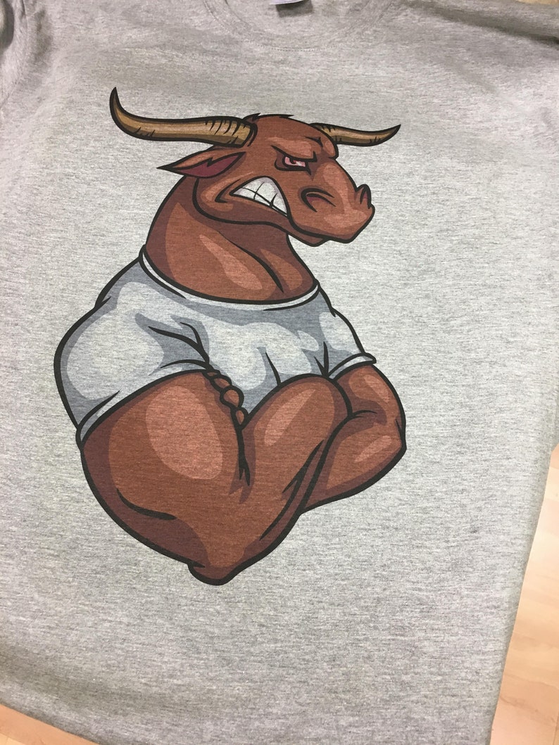 May include: A gray t-shirt with a brown cartoon bull with a white undershirt. The bull has a serious expression and is flexing its muscles.