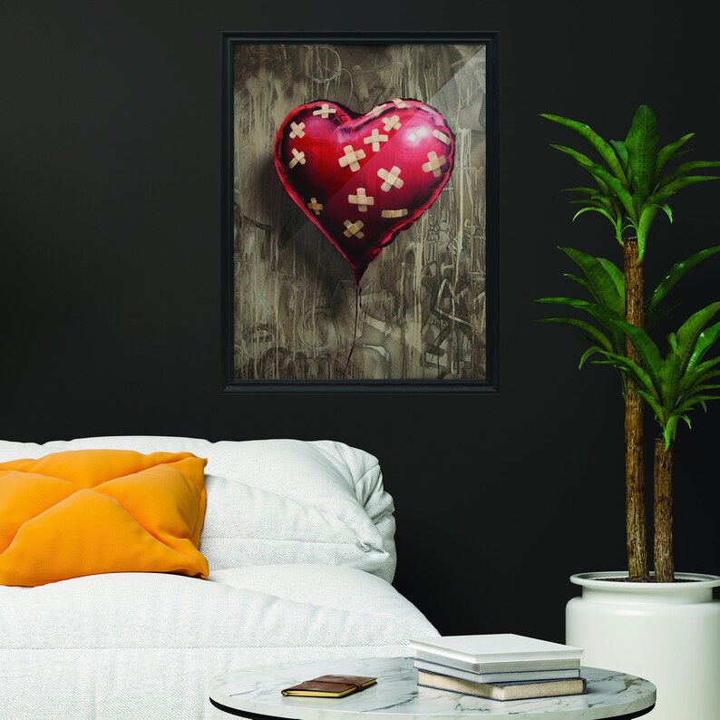 May include: A red heart-shaped balloon with band-aid patches on it, floating against a textured background. The balloon is framed in a black frame.