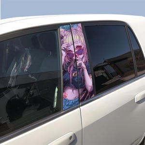 May include: A white car with a window sticker showing a colourful anime-style illustration of a person with pink hair and sunglasses. The artwork is set against a blue sky.
