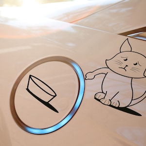 Könnte beinhalten: Ein weißes Auto mit einem schwarz-weißen Aufkleber eines Katers mit traurigem Gesichtsausdruck. Der Kater steht neben einem schwarz-weißen Aufkleber einer Schüssel.