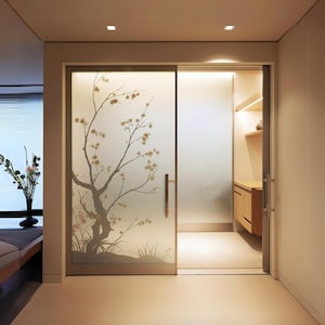 Puede incluir: Una puerta corredera de vidrio esmerilado con un diseño floral que presenta un árbol con ramas y flores. La puerta está abierta, revelando una pequeña habitación con un estante y un armario de madera.
